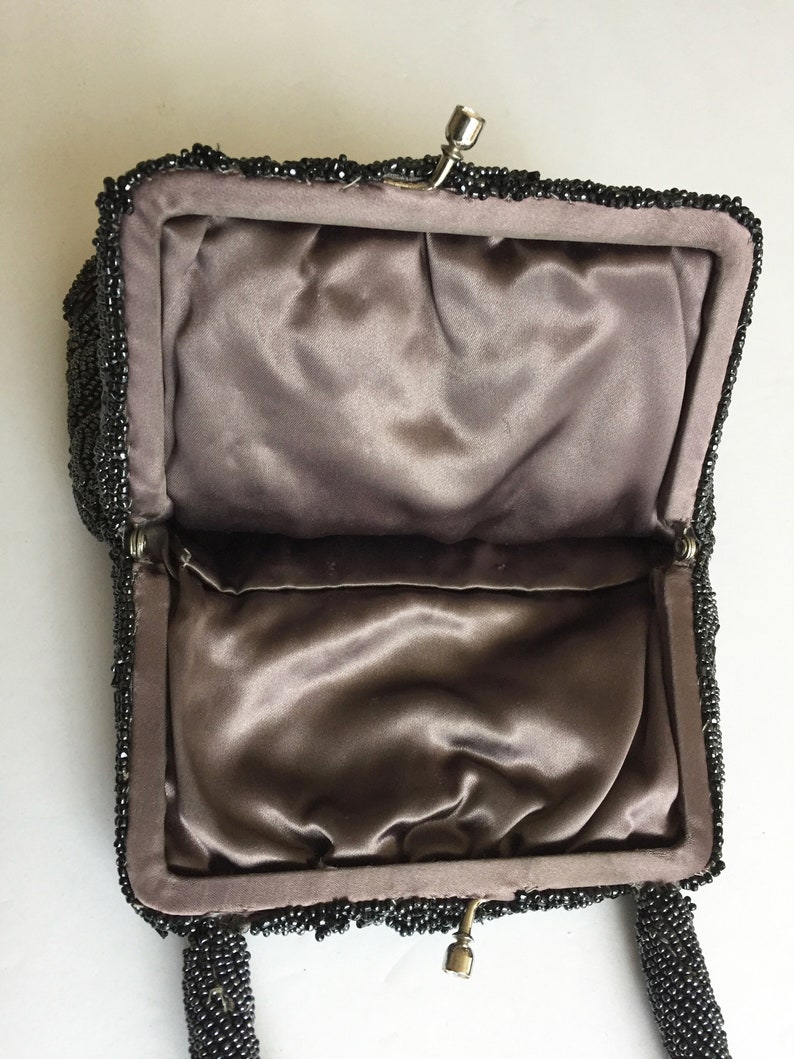 Peut inclure: Un sac &agrave; main de soir&eacute;e noir en perles avec une doublure en satin et une fermeture &agrave; fermoir. Le sac a une courte poign&eacute;e.