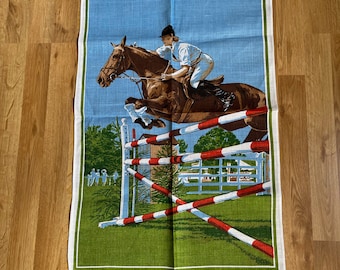 May include: A vintage linen tea towel featuring a colorful illustration of a horse jumping over a fence. The text "Show Jumpers by Lilster" is printed at the bottom of the towel.