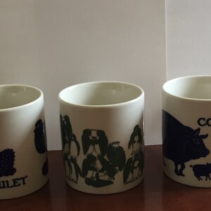 May include: Three white ceramic mugs with blue illustrations and text. One mug features a chicken with the text "LE POULET". Another mug has a group of penguins. The third mug displays a cow, pigs, and the word "COCHON".