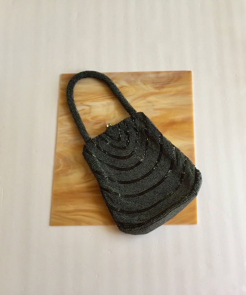 Peut inclure: Un petit sac &agrave; main en perles gris fonc&eacute; avec un design incurv&eacute;. Le sac a une poign&eacute;e sup&eacute;rieure et une fermeture &agrave; fermoir.