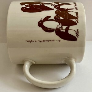 May include: Cream-colored ceramic mug featuring a repeating pattern of brown penguins. The mug has a curved handle and the text "Taylor & Co." is printed near the bottom. A charming and whimsical design for a coffee or tea cup.