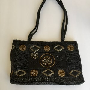 Peut inclure: Un sac &agrave; main noir en perles avec des embellissements dor&eacute;s et argent&eacute;s en forme g&eacute;om&eacute;trique. Le sac a deux anses.
