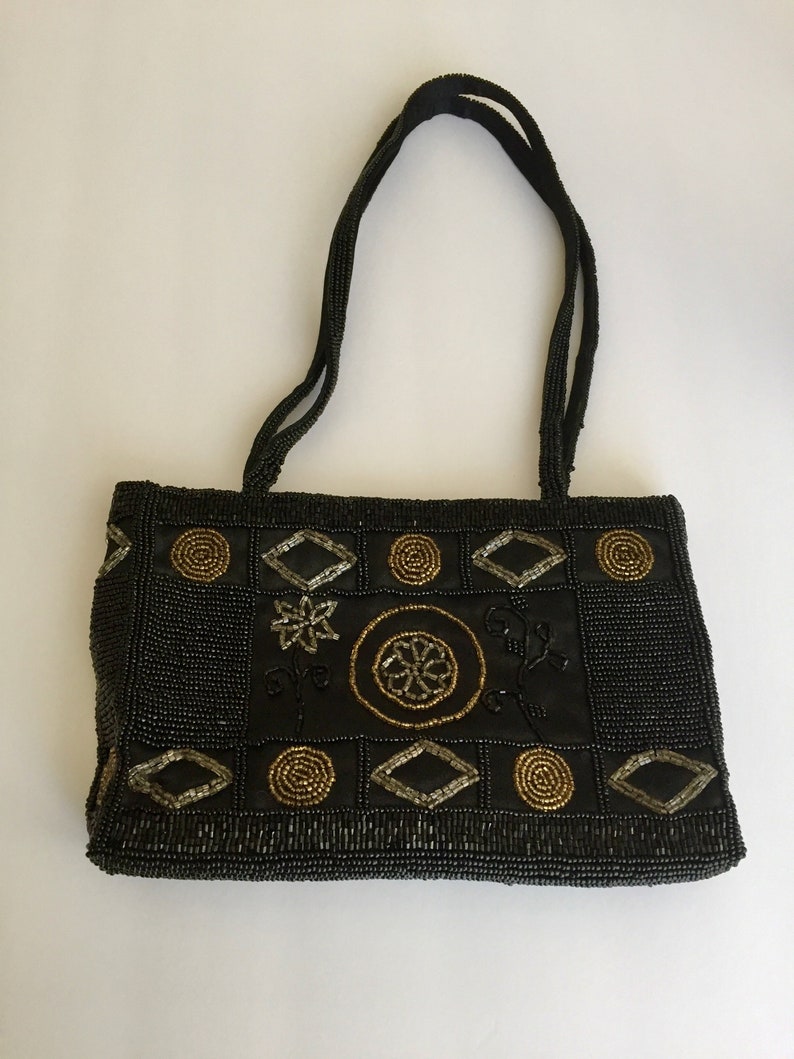 Peut inclure: Un sac &agrave; main noir en perles avec des embellissements dor&eacute;s et argent&eacute;s en forme g&eacute;om&eacute;trique. Le sac a deux anses.
