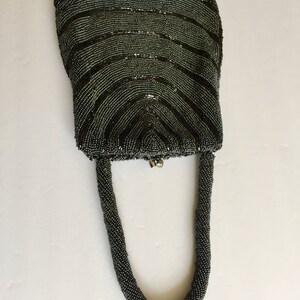 Peut inclure: Un sac &agrave; main de soir&eacute;e gris perl&eacute; avec un dessus incurv&eacute; et une longue anse perl&eacute;e.