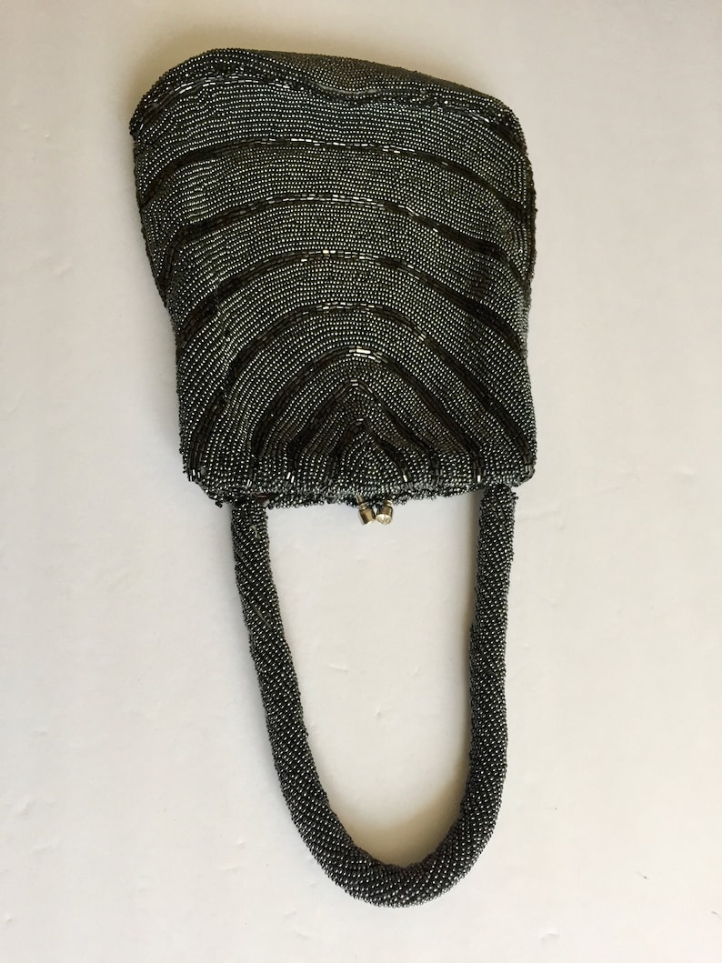 Peut inclure: Un sac &agrave; main de soir&eacute;e gris perl&eacute; avec un dessus incurv&eacute; et une longue anse perl&eacute;e.