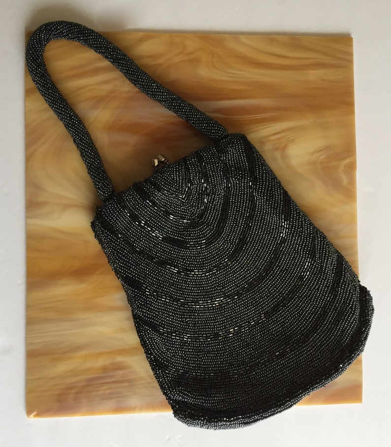 Peut inclure: Un sac &agrave; main de soir&eacute;e noir en perles avec un design incurv&eacute; et une poign&eacute;e sup&eacute;rieure.