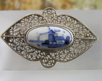 May include: A silver filigree brooch with a blue and white porcelain cameo featuring a windmill scene.