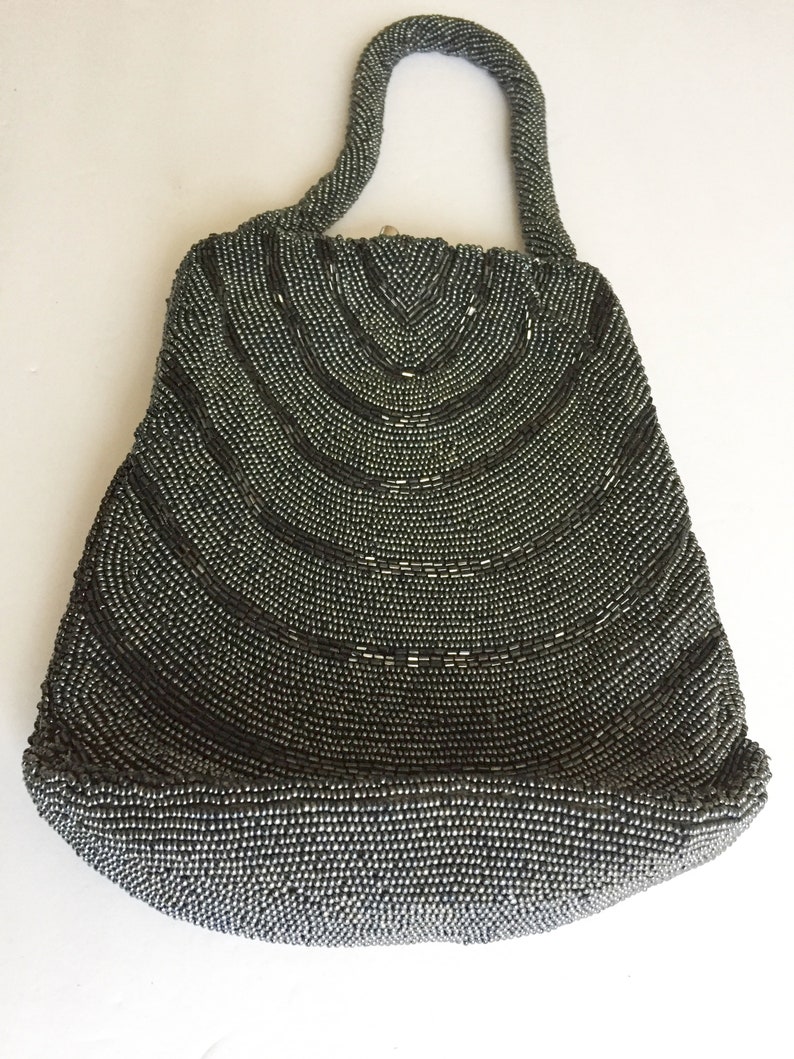 Peut inclure: Un sac &agrave; main de soir&eacute;e gris perl&eacute; avec un design incurv&eacute; et une seule anse sup&eacute;rieure.