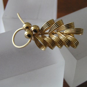 May include: A gold-toned brooch with a leaf design and three round beads. The brooch is made of metal and has a delicate, intricate design.