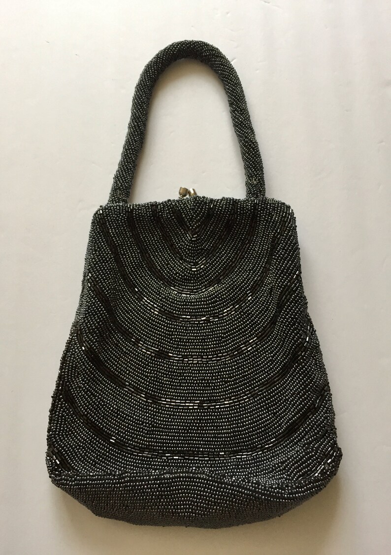 Peut inclure: Un sac &agrave; main de soir&eacute;e gris perl&eacute; avec un design incurv&eacute; et une fermeture &agrave; fermoir sur le dessus.