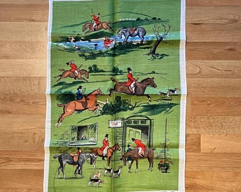 May include: Green and white linen tea towel with a hunting scene illustration. The illustration depicts riders on horseback, dogs, and a building. The word "HUNTING" is printed at the bottom of the towel.
