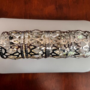 May include: Silver metal napkin rings with an openwork design. The rings have a geometric pattern with a series of connected shapes. The napkin rings are displayed on a white surface against a dark brown background.