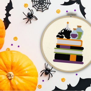 May include: A black cat sitting on a stack of books with a potion bottle and a candle on top. The books are purple, green, orange, and black. The background is white.