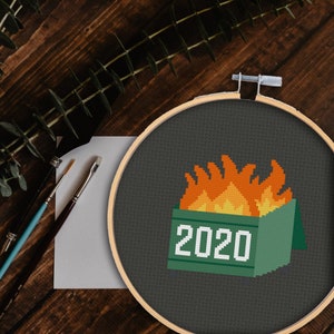 以下が含まれることがあります： 側面に2020年が印刷された緑色のゴミ箱が燃えている。ゴミ箱は濃い灰色の背景にある。