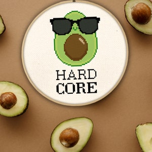 May include: A white embroidery hoop with a green avocado wearing sunglasses and the text "HARD CORE". The avocado is surrounded by four whole avocados.