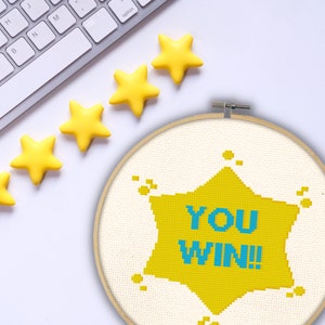 May include: A yellow star-shaped embroidery hoop with the text "YOU WIN!" in blue lettering. Five yellow stars are arranged in a row above the hoop.