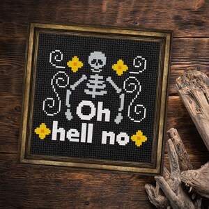 May include: Framed cross-stitch art with a black background and a skeleton design. The text "Oh hell no" is stitched in white. Yellow and white accents complete the Halloween-themed artwork, framed in a gold-colored frame.