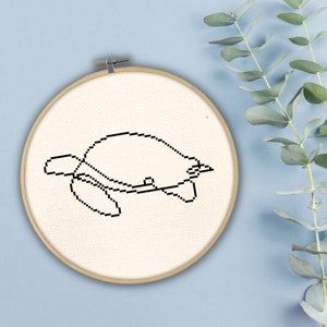 May include: A white embroidery hoop with a black line drawing of a turtle on a white fabric background.
