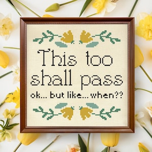 Puede incluir: Un diseño de punto de cruz enmarcado con fondo blanco y marco marrón. El diseño presenta un borde floral verde con flores amarillas y el texto "This too shall pass ok... but like... when?"