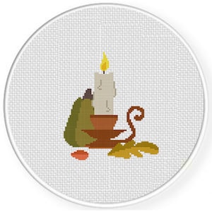 May include: A white candle with a yellow flame sits in a brown ceramic holder. A green gourd and brown leaves are arranged around the candle.