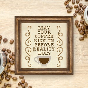 Könnte beinhalten: Ein brauner Holzrahmen mit weißem Hintergrund und braunem Text, der "May your coffee kick in before reality does" lautet. Eine braune Kaffeetasse mit weißem Umriss befindet sich in der Mitte des Textes.