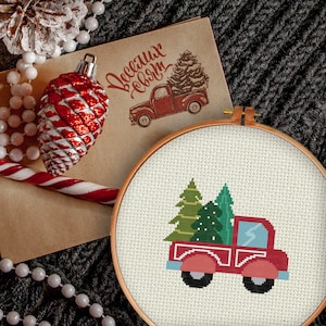 Peut inclure: Un camion rouge avec une cabine et une benne blanches transporte deux sapins de Noël verts. Le camion est sur un fond blanc avec une bordure blanche.