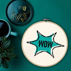 May include: A white embroidery hoop with a blue and white starburst design that says "WOW" in black letters.