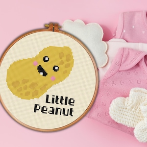 May include: A white embroidery hoop with a yellow peanut with a smiling face and the text "Little Peanut".
