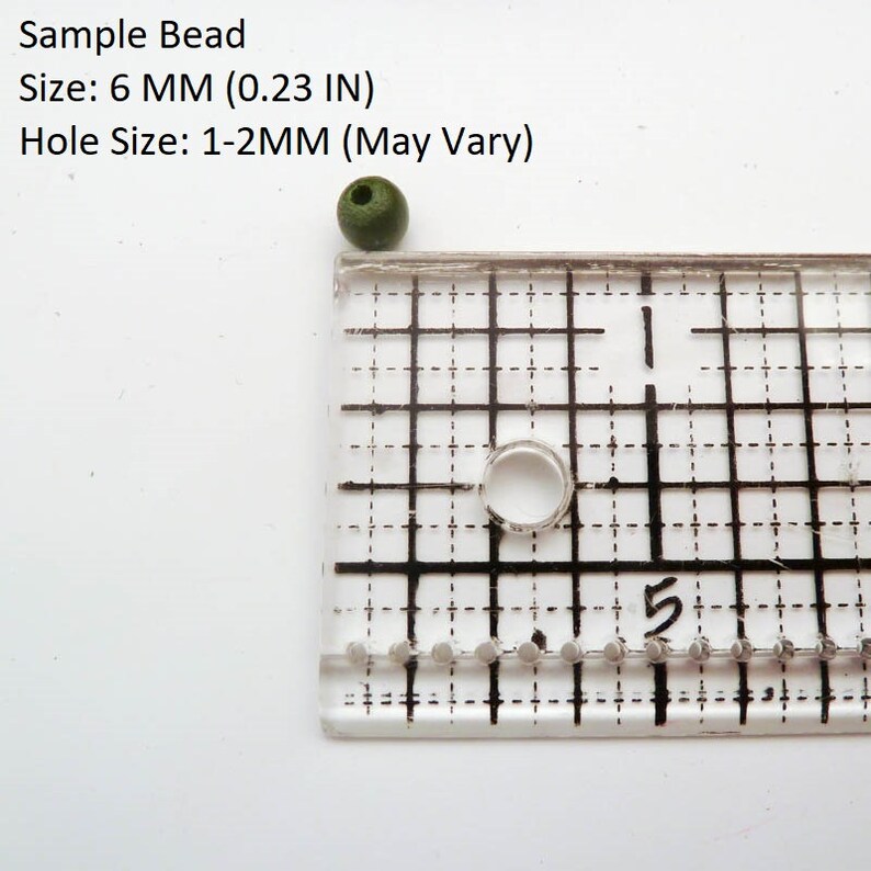 May include: A dark green round bead with a hole in the center, measured against a ruler. The bead is 6 mm (0.23 inches) in diameter. The hole size is 1-2 mm.  Sample Bead. Size: 6 MM (0.23 IN). Hole Size: 1-2MM (May Vary).