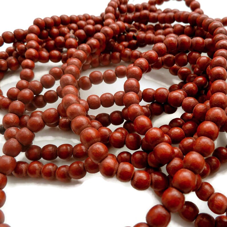 May include: A strand of dark red wooden beads. The beads are round and smooth, and they are strung together on a thin cord. The beads are arranged in a loose pile, and they are illuminated by a bright light.