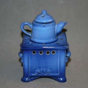 May include: A blue ceramic teapot with a lid sits on top of a blue ceramic stove with a decorative design. The stove has holes on the sides and a decorative design on the front.