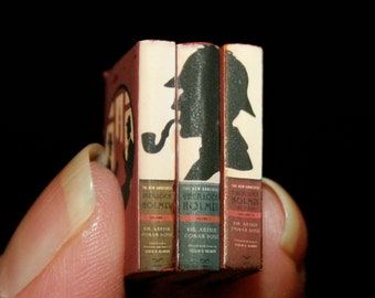 May include: Three miniature hardcover books with red, brown, and gold covers. The books are titled "The New Adventures of Sherlock Holmes" and feature a silhouette of Sherlock Holmes on the cover.