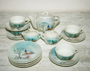 May include: A vintage porcelain tea set with a winter scene design. The set includes a teapot, creamer, sugar bowl, four cups, and four saucers. The cups and saucers have a blue and white snowflake pattern with a winter village scene.