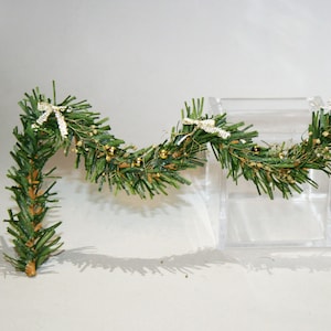 May include: A green garland with gold bells and white bows. The garland is draped over a clear acrylic block.