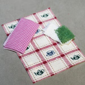 May include: A white and red checkered fabric with a green patch and a pink patterned fabric. The fabric has a design of teacups and teapots.