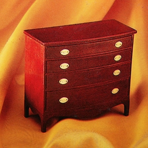 May include: A mahogany chest of drawers with five drawers and brass pulls. The chest is on a yellow fabric background.