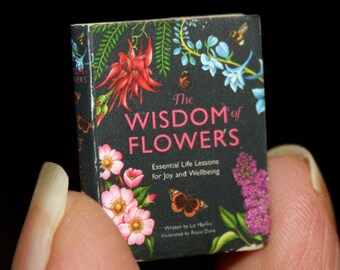 May include: A book titled "The Wisdom of Flowers: Essential Life Lessons for Joy and Wellbeing" with a floral design on the cover. The cover features pink, white, and blue flowers, green leaves, and a butterfly.