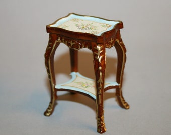 May include: A miniature wooden table with a white and gold painted top and a lower shelf. The table has ornate carvings and a light brown finish.