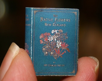 May include: A miniature blue book with gold lettering titled "The Native Flowers of New Zealand" by Mrs. Charles Hetley. The cover features a colorful illustration of native flowers.