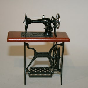 May include: A miniature black sewing machine with a wooden tabletop and ornate metal base. The machine features a silver hand wheel and a foot pedal. The sewing machine is a vintage style, likely a collectible or decorative item.