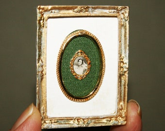 May include: A small, ornate gold frame with a green oval mat and a black and white portrait of a woman inside. The frame has a white background and is decorated with gold accents.