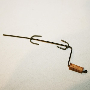 Puede incluir: Una brocheta de metal con mango de madera. La brocheta tiene dos puntas en cada extremo y se utiliza para asar alimentos sobre el fuego.