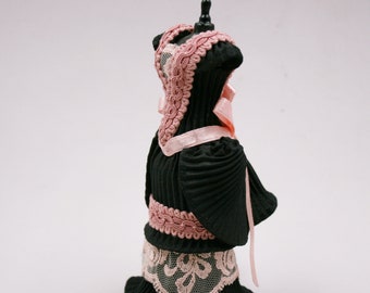 May include: A black dress with pink lace trim and a pink ribbon bow. The dress is on a mannequin and has a pleated skirt.