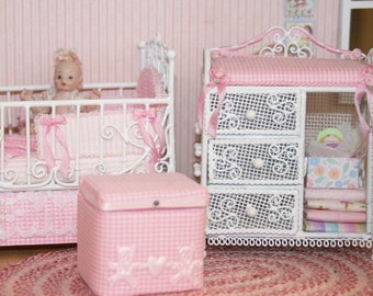 Könnte beinhalten: Weißes Weidenkörbchen-Puppenmöbelset mit rosa Gingham-Stoff. Das Set beinhaltet ein Kinderbett, eine Wickelkommode, einen Schaukelstuhl und eine Aufbewahrungskiste. Alle Teile sind mit weißer Spitze verziert.