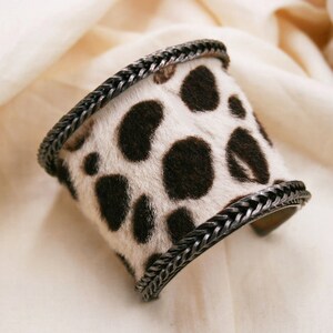 May include: A black and white animal print cuff bracelet with a silver metal chain detail.
