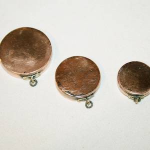 Peut inclure: Trois pendentifs ronds en cuivre avec une finition brillante et une petite boucle en bas pour la suspension.