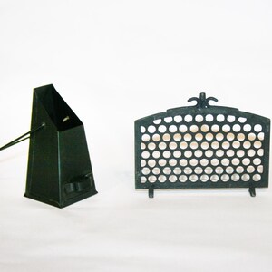May include: Two dark green metal fireplace accessories. One is a tall, angular coal scuttle with a handle. The other is a decorative screen with a series of circular cutouts and a curved top.