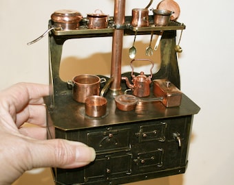 May include: A miniature copper and brass stove with a chimney and multiple pots and pans. The stove has two ovens with doors and a shelf above for storage.