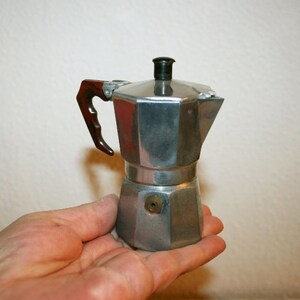 Puede incluir: Una cafetera de espresso de acero y negro con un mango de madera. La cafetera está sentada en la mano de una persona.