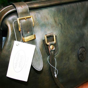 May include: Dark green leather handbag with gold-colored buckles and a tag that reads "valentino orlandi". The bag has a structured shape with a top handle and a shoulder strap. The leather has a slightly distressed appearance.